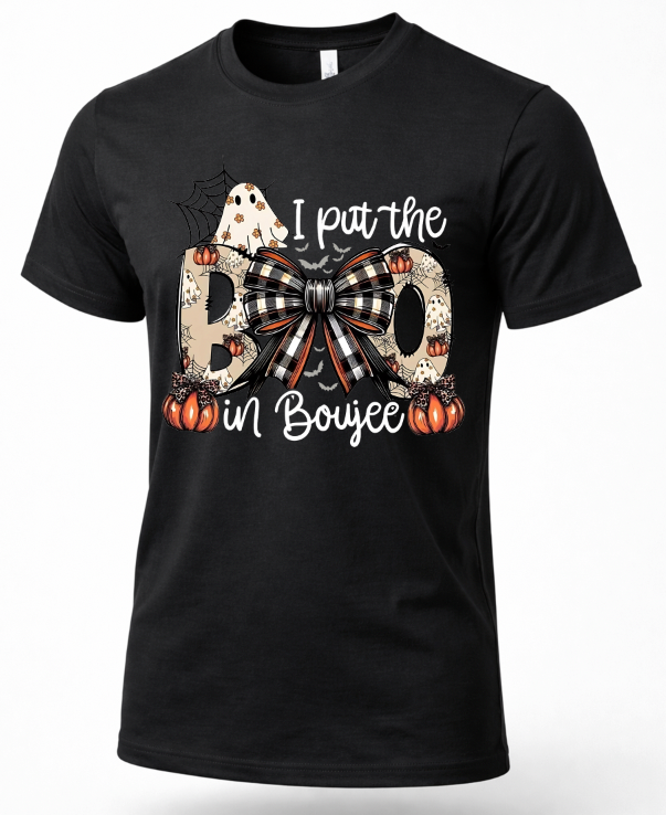 A black short-sleeve crewneck t-shirt featuring a Halloween-themed graphic print on the front. The graphic reads 'I put the BO in Boujee' with the letters 'B' and 'O' styled as patterned pillows with a large black-and-white buffalo plaid bow in the center, flanked by orange pumpkins, a white ghost, and a spiderweb.