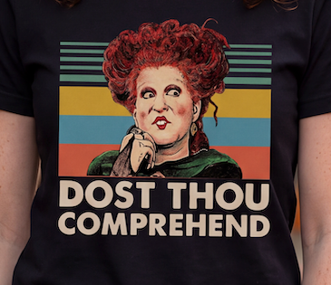 A close-up of a person wearing a black graphic T-shirt. The shirt features a stylized illustration of a woman with red hair and the text 'DOST THOU COMPREHEND' in bold cream lettering, set against a retro striped background.