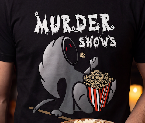 A close-up of a person wearing a black t-shirt with a graphic print that reads 'MURDER SHOWS' in a dripping white font above a gray cartoon character eating popcorn from a red-and-white striped bucket.