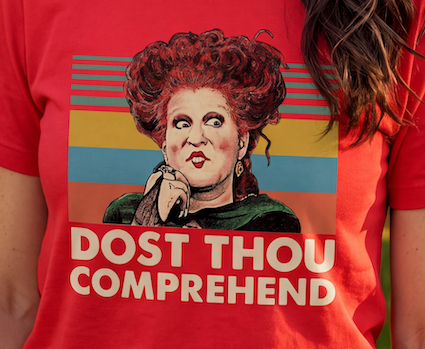 A close-up of a person wearing a bright red graphic T-shirt. The shirt features a stylized portrait of a woman with curly red hair and the text 'DOST THOU COMPREHEND' in large white letters over a striped rectangular background.