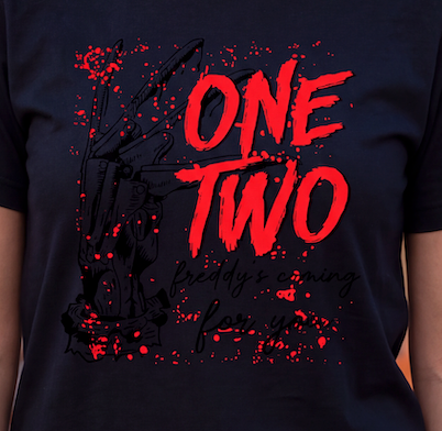 A close-up of a person wearing a dark navy T-shirt with a large horror-style graphic. The design features the words 'ONE TWO' in bold red brush lettering, with smaller red and black script text below reading 'freddy's coming for you,' plus a black illustrated claw machine and red paint splatter details.