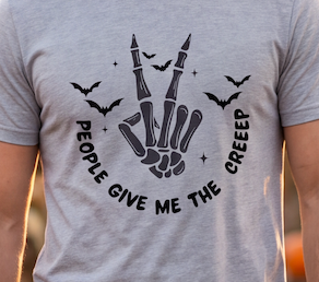 A close-up of a person wearing a heather gray t-shirt with a black graphic of a skeletal hand making a peace sign, surrounded by bats and the text 'PEOPLE GIVE ME THE CREEP'.