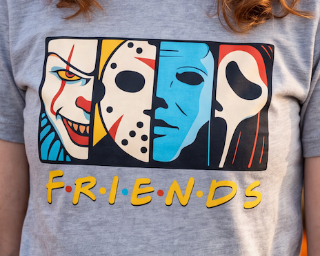 A close-up of a person wearing a heather gray t-shirt with a graphic print of horror movie villains styled like the Friends logo, featuring the word 'FRIENDS' in yellow with red and blue dots.