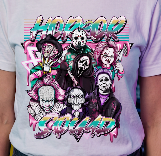 A close-up of a person wearing a light lavender-purple t-shirt with a colorful graphic print featuring horror movie villains and the text 'HORROR SQUAD'.