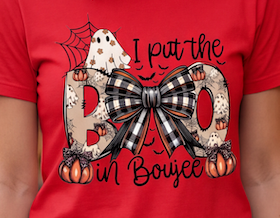 A close-up of a red short-sleeve T-shirt featuring a Halloween graphic with the phrase 'I put the BOO in Boujee.' The design includes a black-and-white gingham bow, patterned letters, pumpkins, bats, and a ghost.