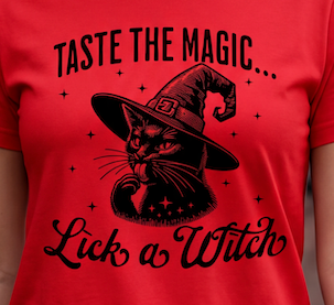 A close-up of a red short-sleeve T-shirt with a black graphic print of a witch cat wearing a pointed hat, with the text 'TASTE THE MAGIC.