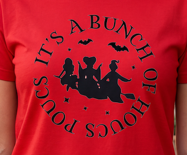 A close-up of a red short-sleeve T-shirt worn by a person, featuring a large black circular graphic with the phrase 'IT'S A BUNCH OF HOCU POCUS' and silhouettes of three witches on a broomstick with bats.
