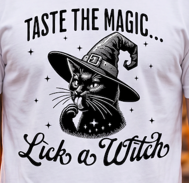 A close-up of a white T-shirt featuring a black graphic of a witch cat wearing a pointed hat, with the text 'TASTE THE MAGIC.