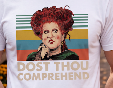 A close-up of a white t-shirt featuring a retro graphic of the character Black Beauty with red hair and the text 'DOST THOU COMPREHEND' in beige block letters.