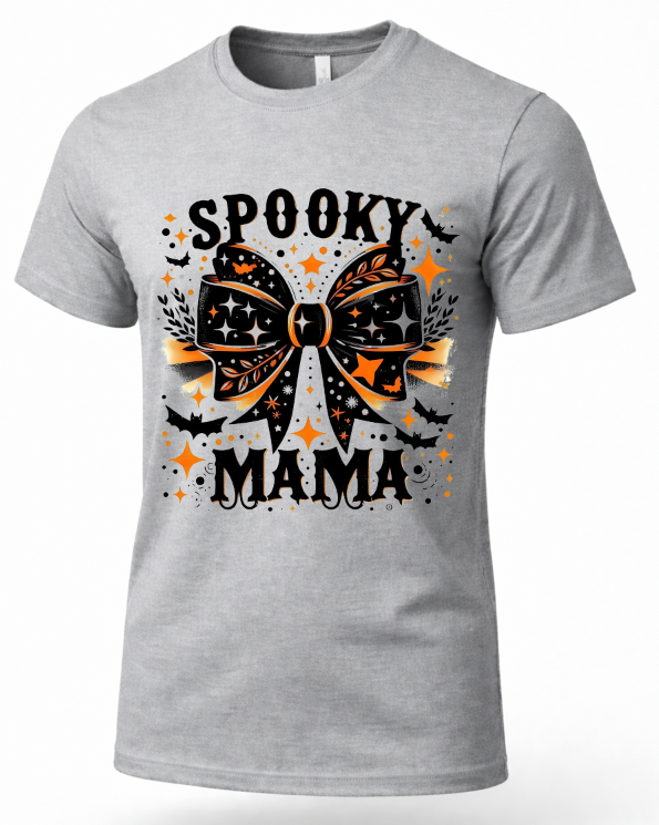 A heather gray short-sleeve crewneck t-shirt featuring a 'Spooky Mama' Halloween graphic on the front. The graphic includes a large black and orange patterned bow, bats, stars, and the text 'SPOOKY MAMA' in black.