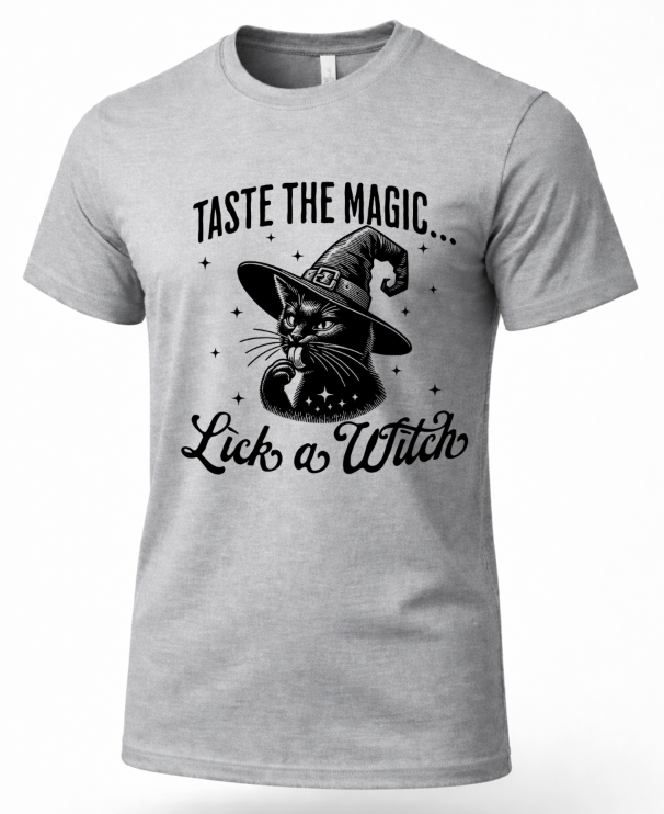 A light gray heather crewneck t-shirt featuring a black graphic print of a witch cat wearing a pointed hat, with the text 'TASTE THE MAGIC.