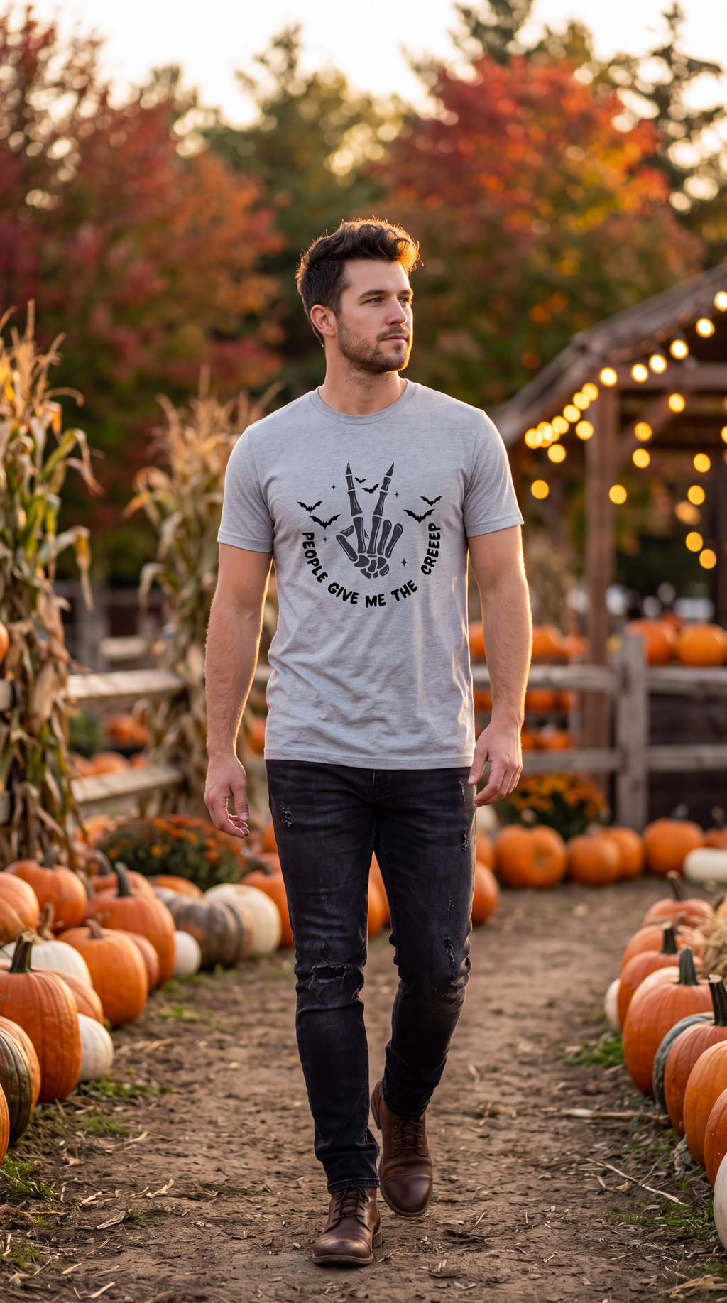 A man walking through a pumpkin patch wearing a light gray t-shirt with a black graphic of a skeleton hand holding a phone and the text 'WHEN IT RAINS, GIVE ME THE RAIN'.