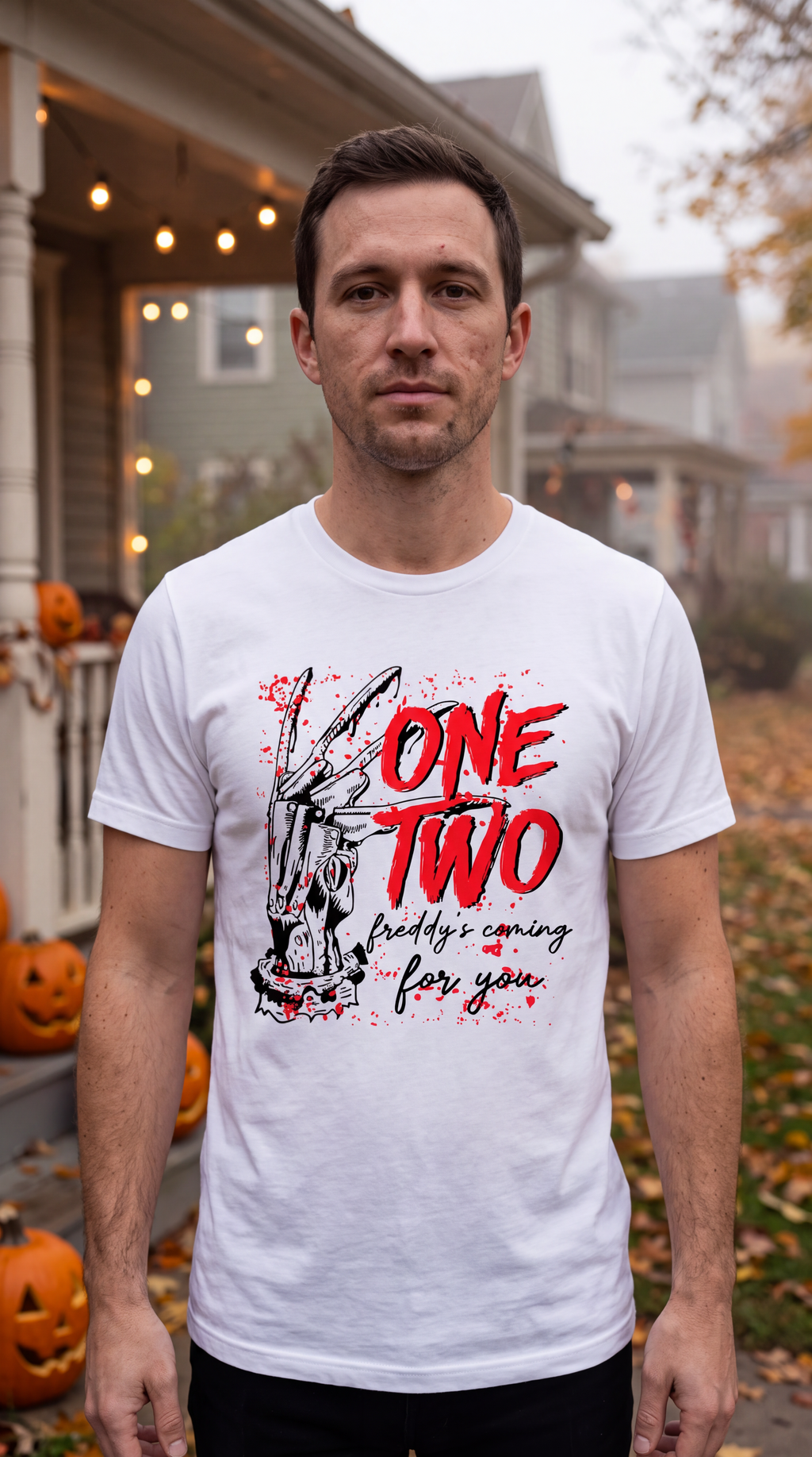 A man wearing a white graphic t-shirt with a horror-themed design featuring a zombie and the text 'ONE TWO Freddy's coming for you', standing in front of a house decorated for Halloween.