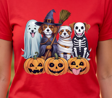 A red short-sleeve T-shirt featuring a colorful graphic of four dogs dressed in Halloween costumes with three jack-o'-lantern pumpkins below them, shown on a model.