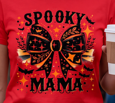A red short-sleeve T-shirt with a large Halloween graphic reading 'SPOOKY MAMA' and a bow design, shown on a person holding a coffee cup. The visible person/body parts are cropped, but the shirt is the product focus.