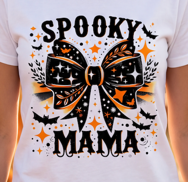 A white short-sleeve T-shirt worn by a person, featuring a large Halloween graphic with the words 'SPOOKY MAMA' and a decorative bow in black and orange with star and bat motifs.