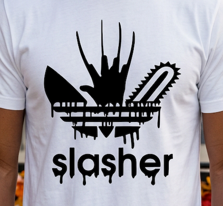 A white short-sleeve t-shirt featuring a black graphic of a dripping chainsaw and the word 'slasher' below it, worn by a person.