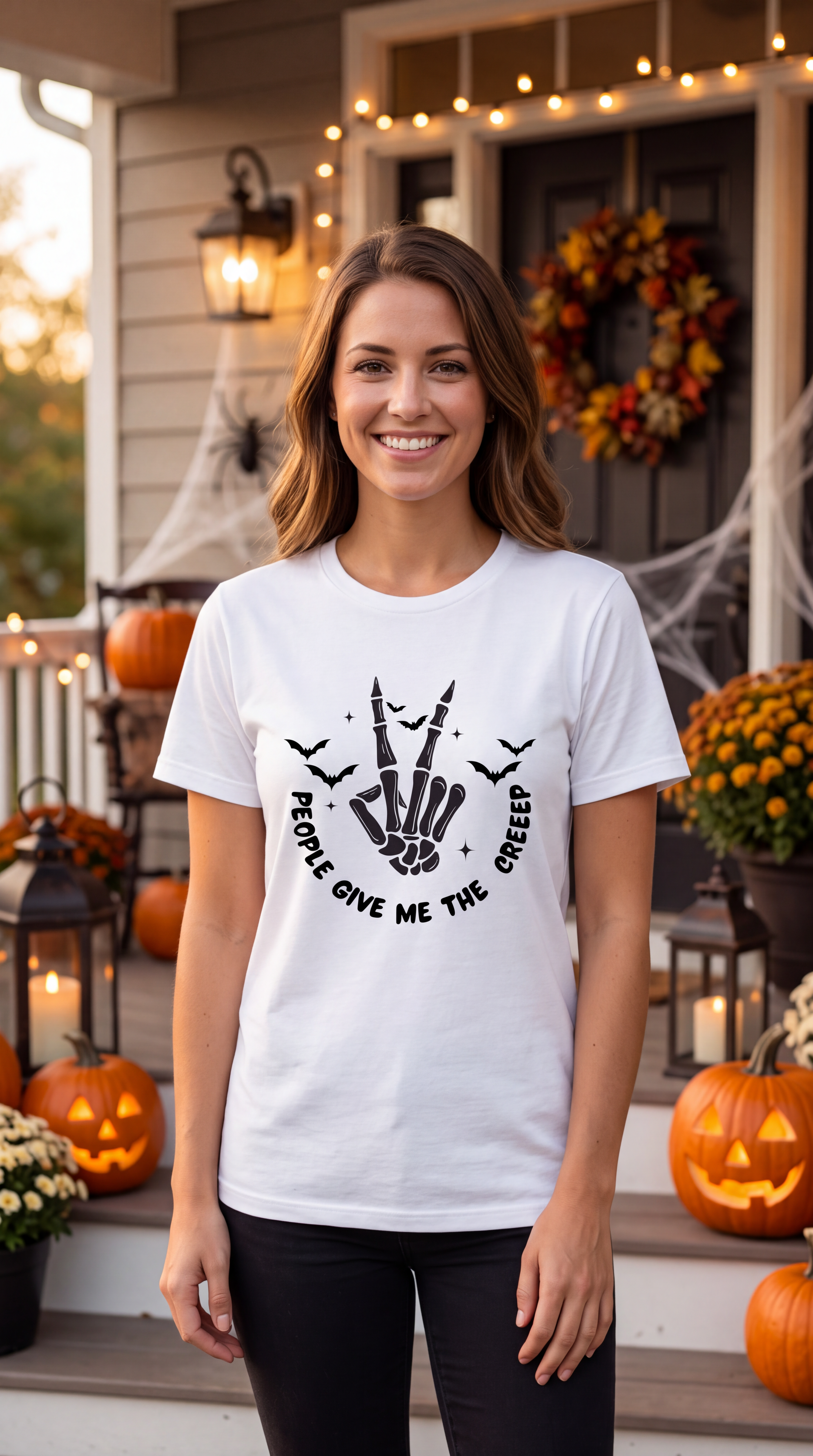 A woman stands on a decorated Halloween porch wearing a white graphic T-shirt with a black skeleton hand design and the text 'PEOPLE GIVE ME THE CREEP'.