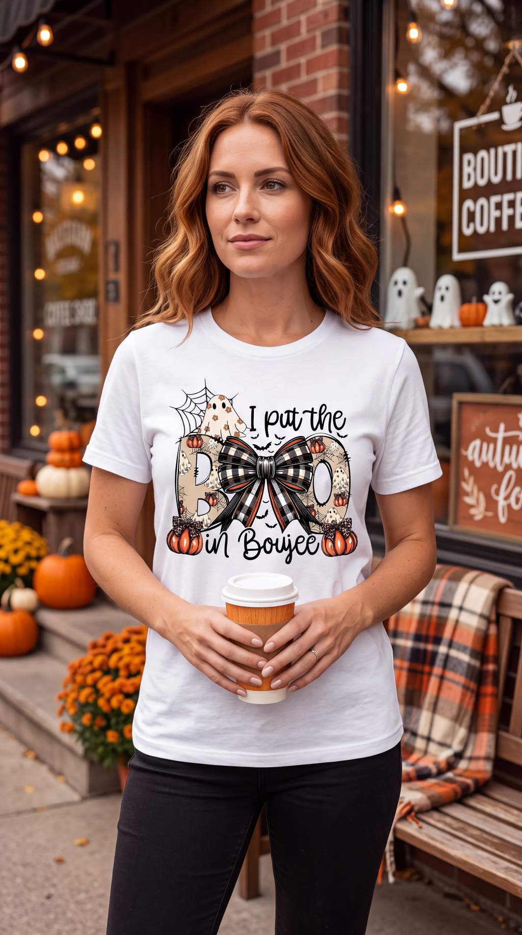 A woman wearing a white short-sleeve crewneck t-shirt featuring a Halloween graphic print on the front. The graphic reads 'I pat the BO in Boujee' with the letter 'O' styled as a large black-and-beige plaid bow, flanked by orange pumpkins, a spiderweb, and a small ghost.