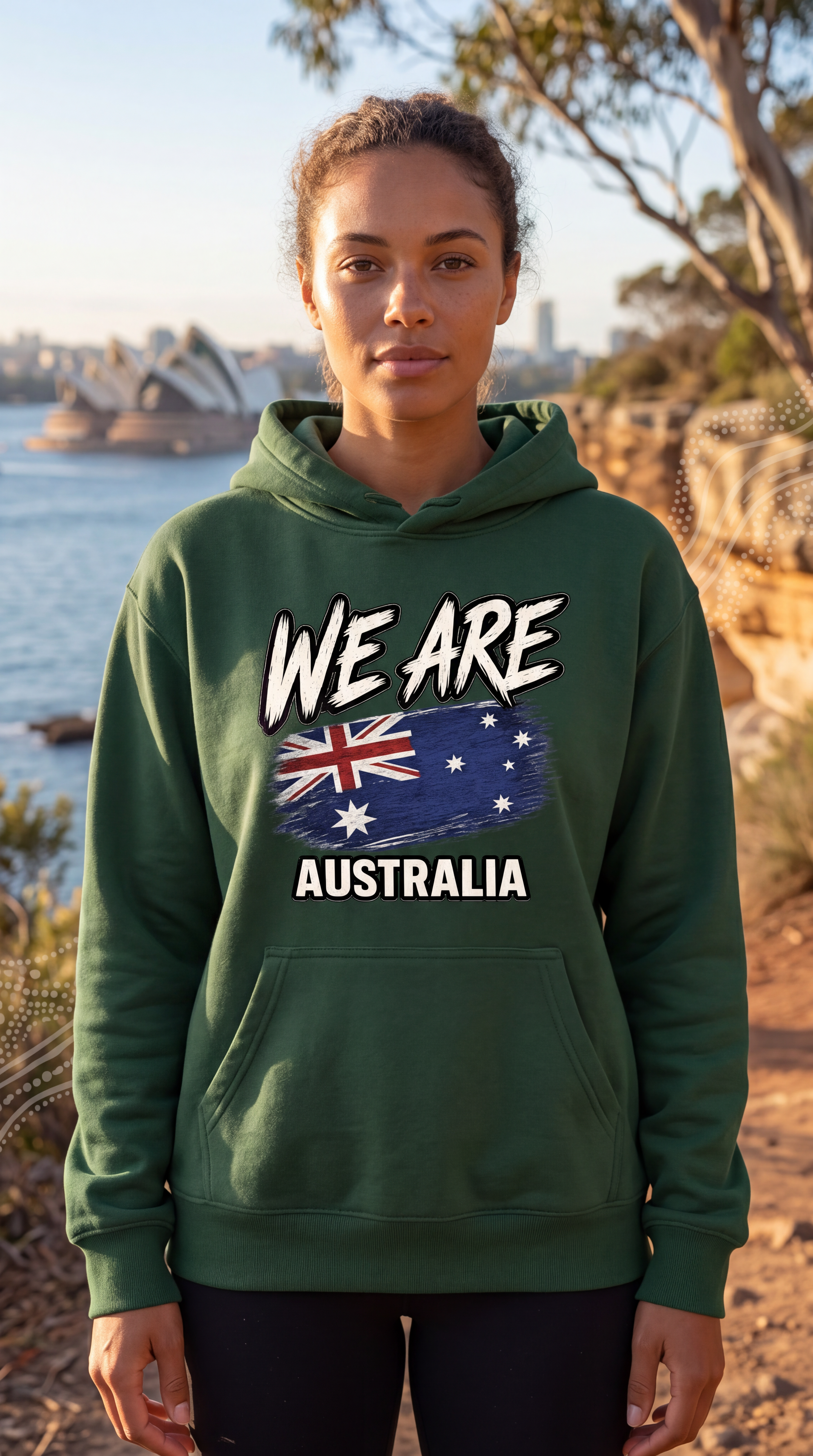 A woman wearing a dark green hoodie with a 'WE ARE AUSTRALIA' graphic featuring the Australian flag, standing outdoors in front of a scenic coastal background.