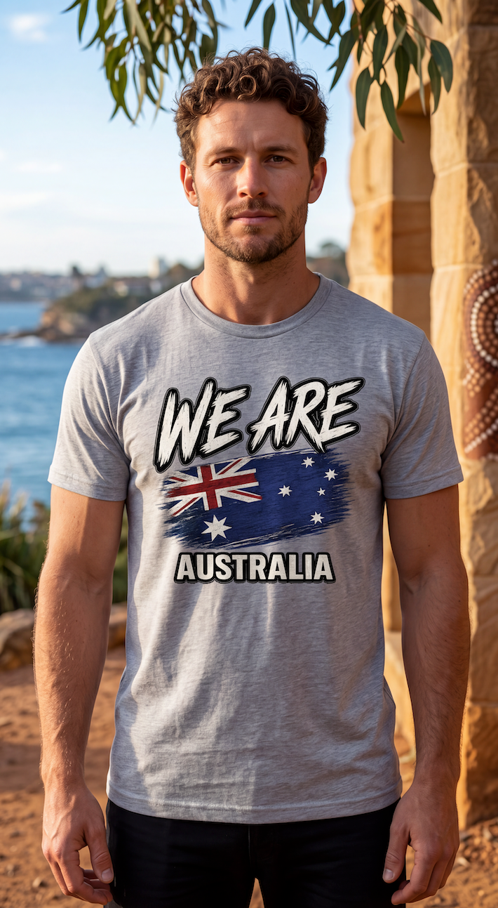 A man wearing a heather gray graphic t-shirt with 'WE ARE AUSTRALIA' and the Australian flag printed on the front, standing outdoors near a stone wall and water.