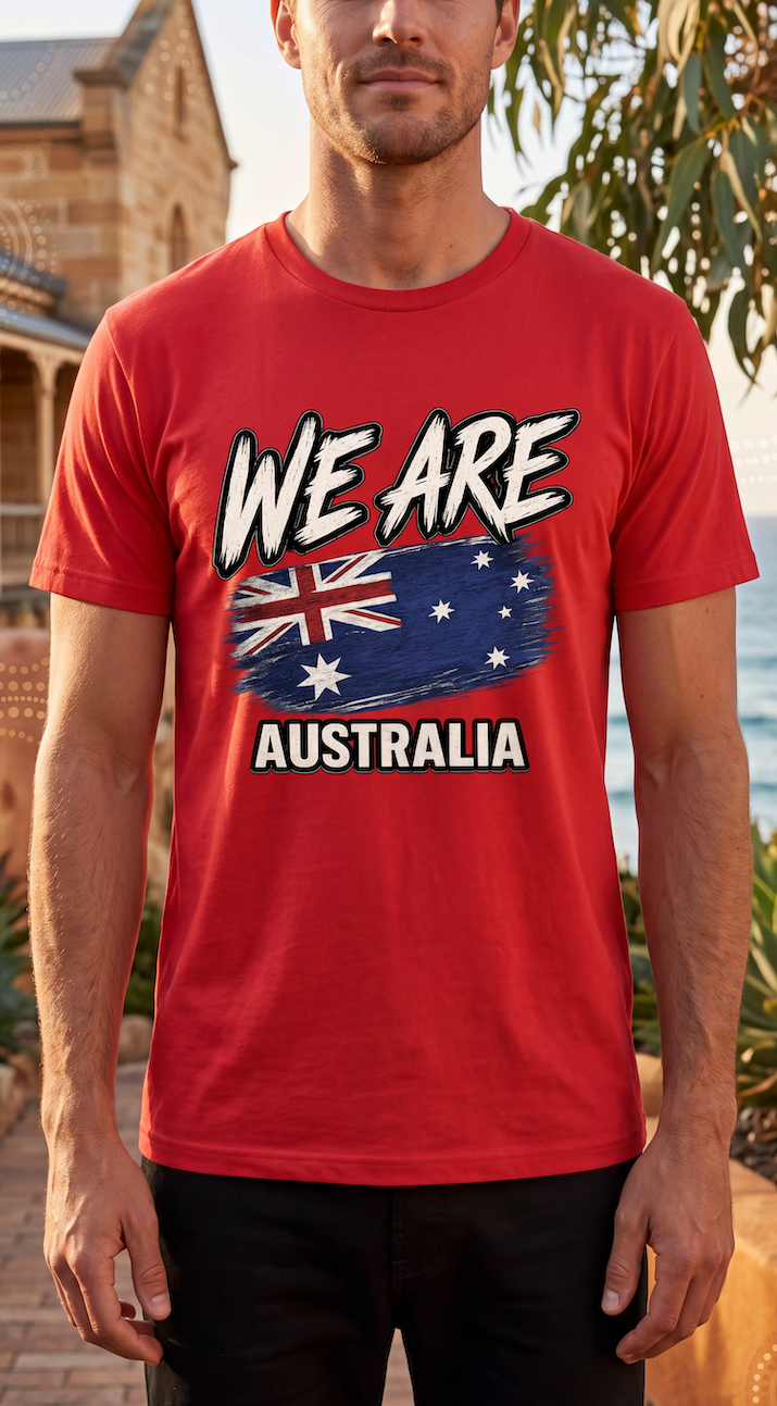 A man wearing a red short-sleeve t-shirt with a graphic print that reads 'WE ARE AUSTRALIA' above and below a stylized Australian flag. The background shows an outdoor beachside setting with blurred trees and a building.