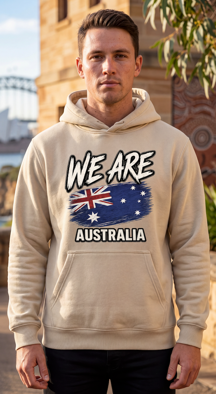 A man wearing a beige hoodie with a graphic print that reads 'WE ARE AUSTRALIA' above and below an Australian flag design, standing outdoors in front of a building.