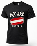 A black short-sleeve crewneck t-shirt featuring a graphic print with the text 'WE ARE' in white brush lettering above a red and white striped flag design, and 'AUSTRIA' printed below in white.