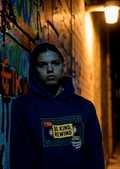 Person wearing blue hoodie with ‘Be Kind Rewind’ cassette graphic in urban alley at night