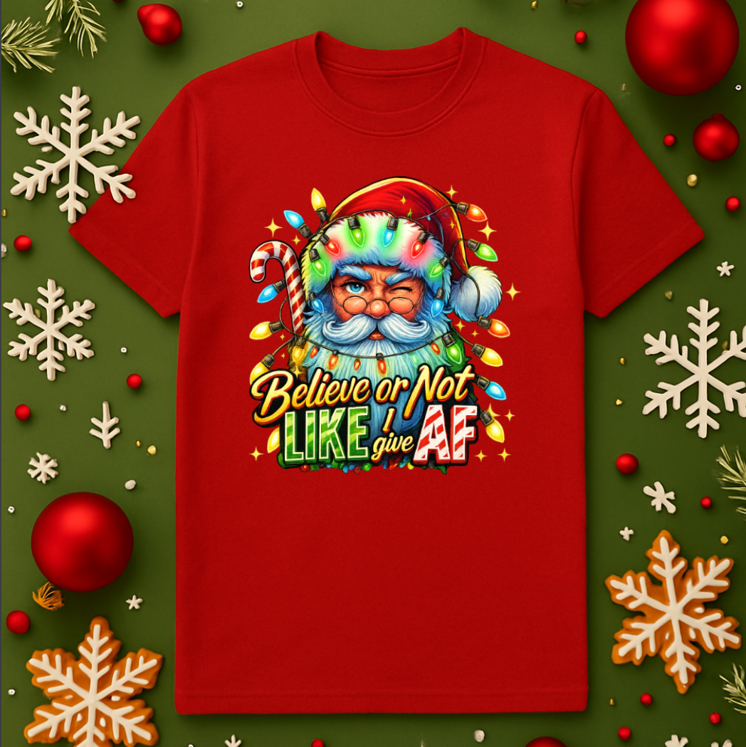 Red Christmas t-shirt featuring a colorful Santa Claus graphic wrapped in holiday lights with the phrase “Believe or Not I Like Give AF,” displayed on a festive green background with ornaments and snowflakes.
