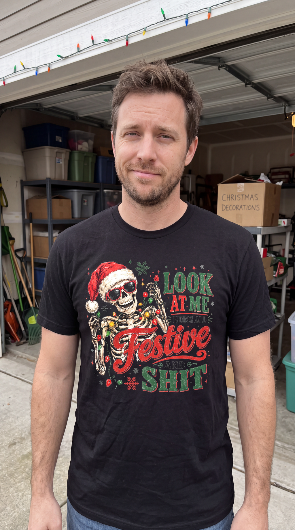 Black lifestyle: Man wearing black Look at Me Being All Festive and Shit Christmas shirt with Santa skeleton and holiday lights graphic.