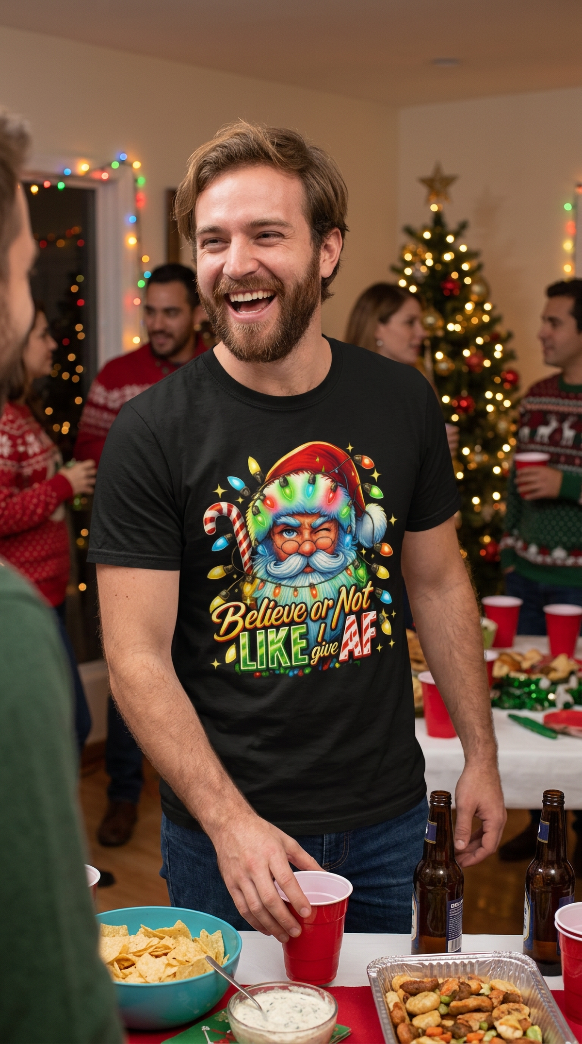 Lifestyle – Black: Man wearing a black Believe or Not Like I Give AF Christmas graphic t-shirt at an indoor holiday party with Christmas decorations.