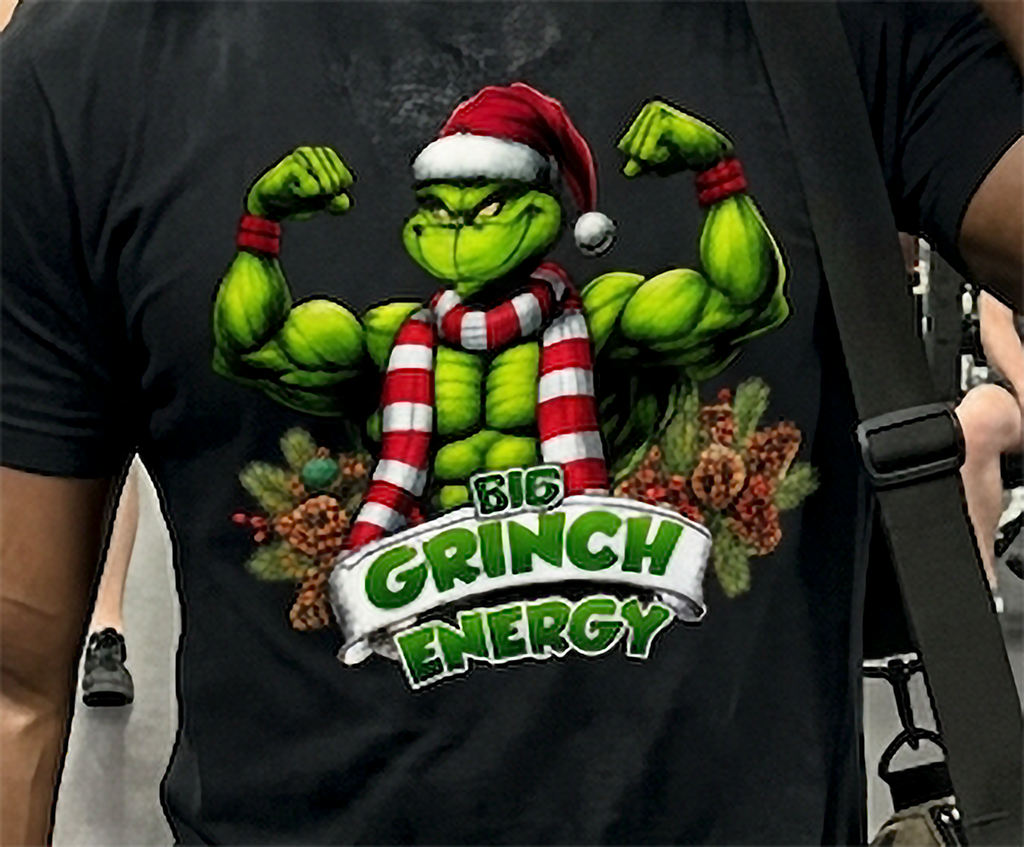 Close-up of Big Grinch Energy Christmas graphic on black t-shirt featuring a muscular green Grinch in a Santa hat and holiday scarf.