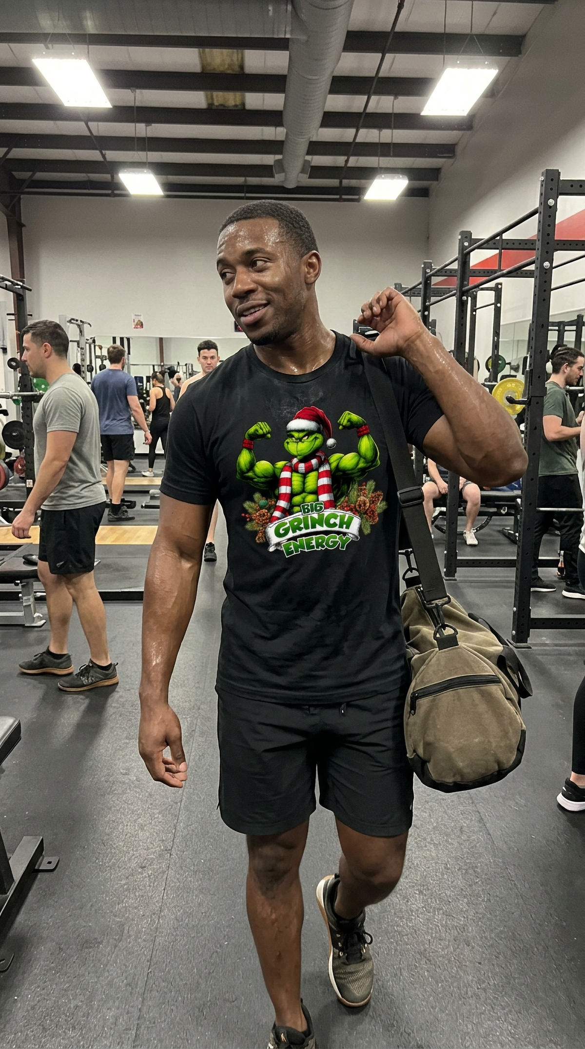 Man wearing black Big Grinch Energy Christmas t-shirt at the gym featuring a muscular green Grinch flexing in a Santa hat and striped scarf.