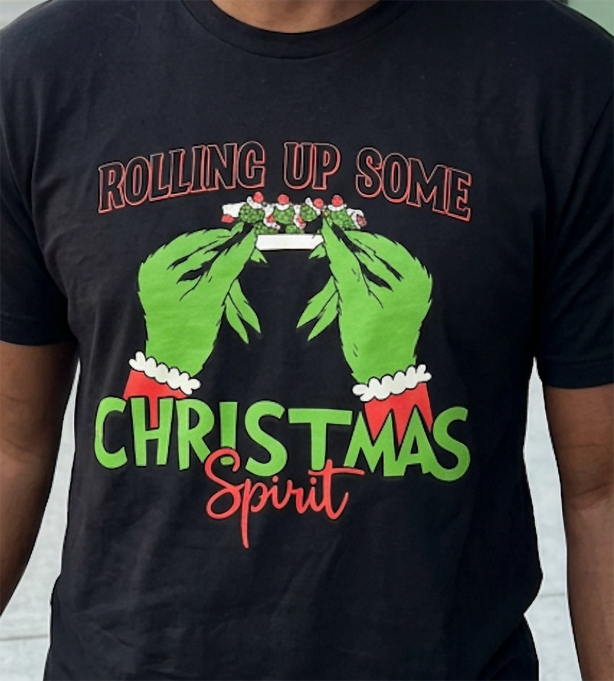 Close-up of black weed Christmas shirt showing green hands, Santa-style sleeves, and cannabis-inspired holiday graphic.