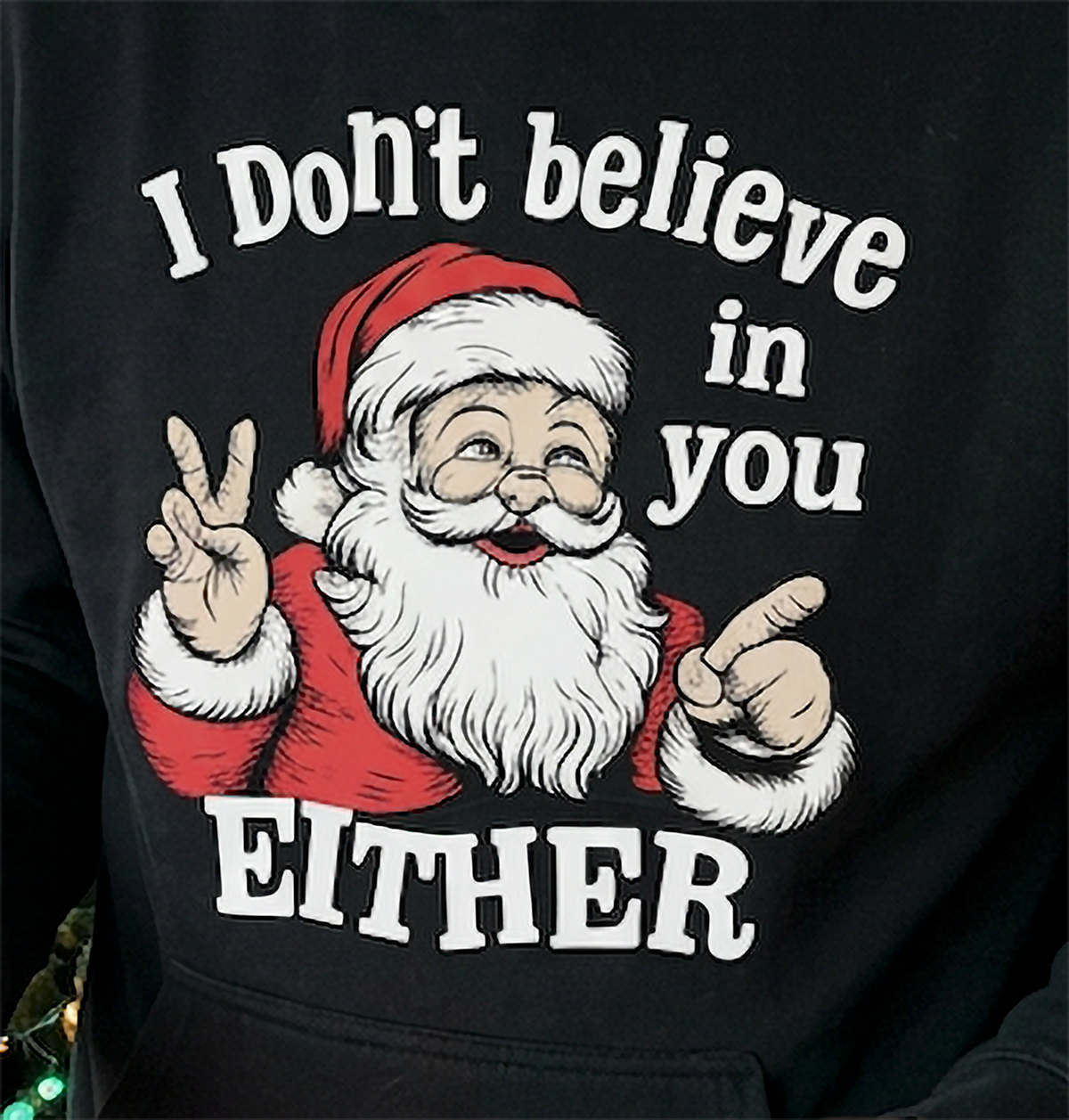 Close-up of I Don’t Believe in You Either Santa graphic on black Christmas hoodie