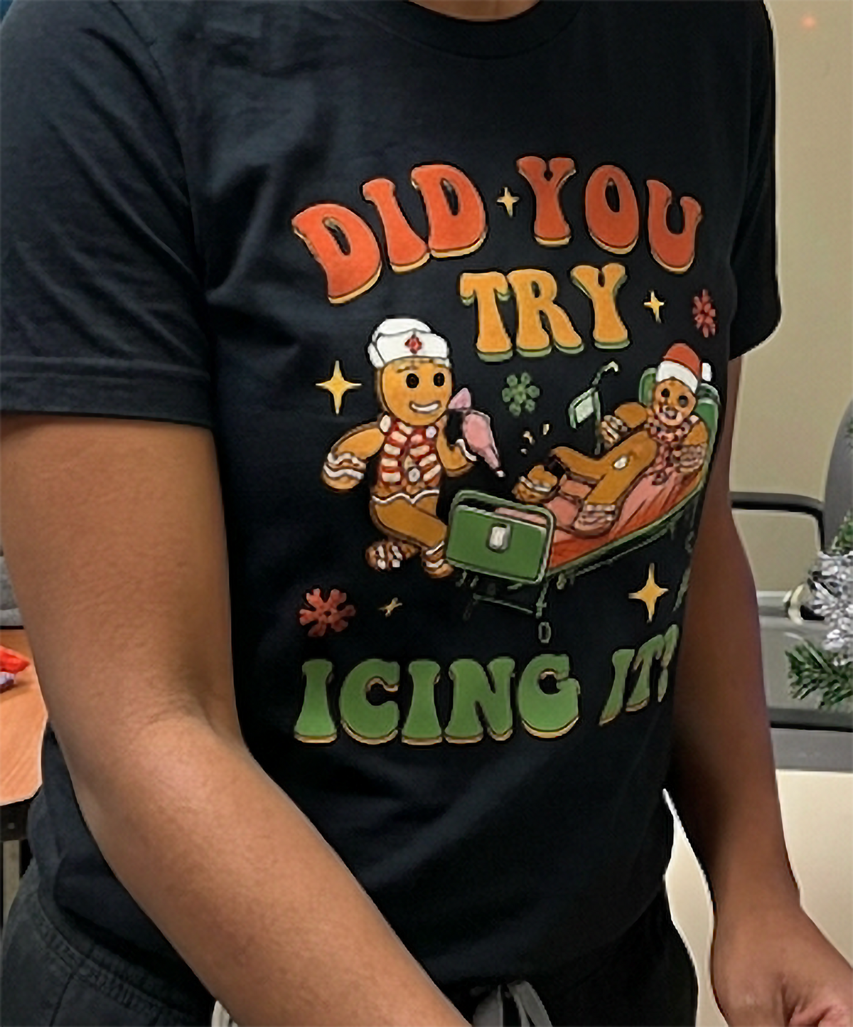 Close-up of funny gingerbread icing Christmas shirt on black fabric, featuring a festive healthcare joke.