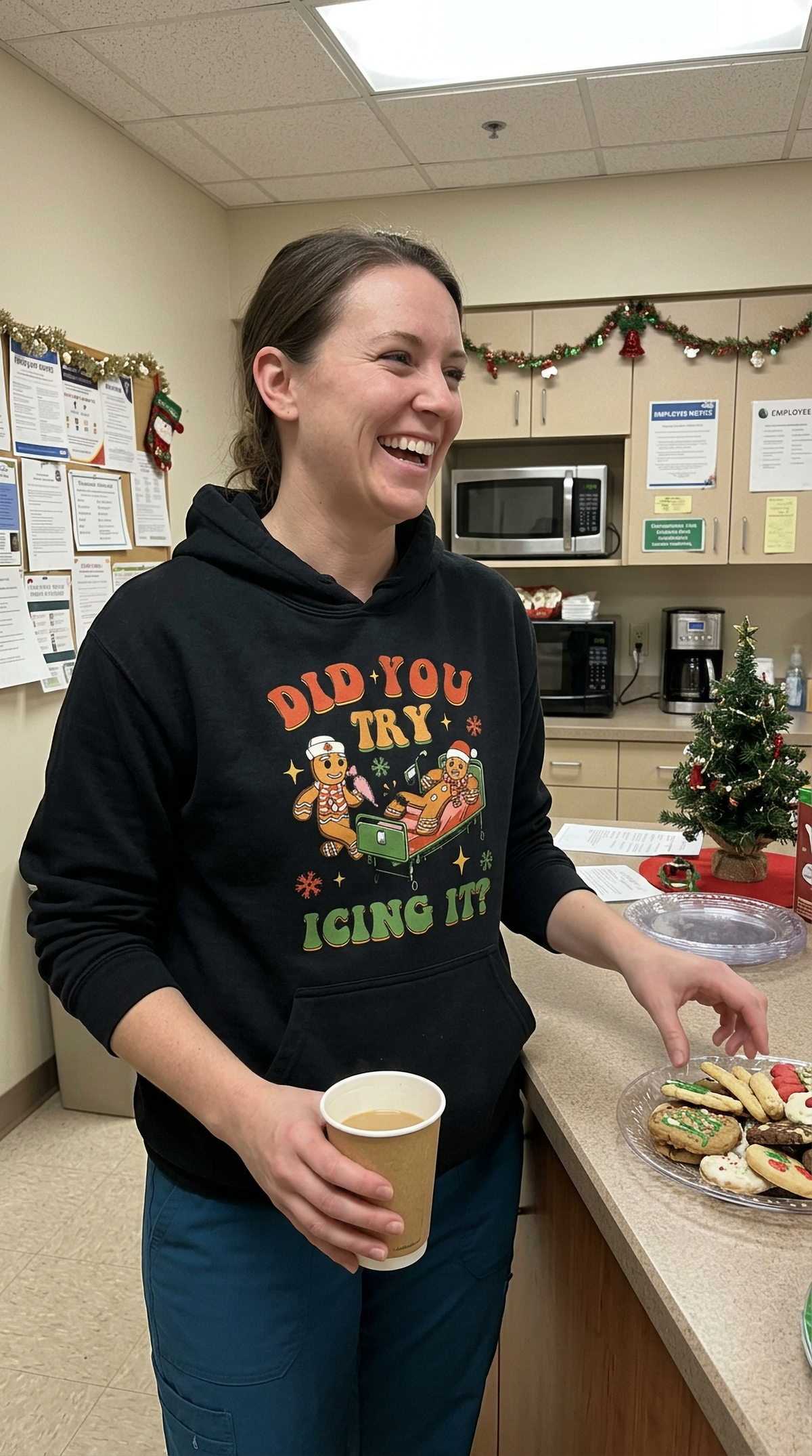Woman wearing black Did You Try Icing It Christmas hoodie in a healthcare setting