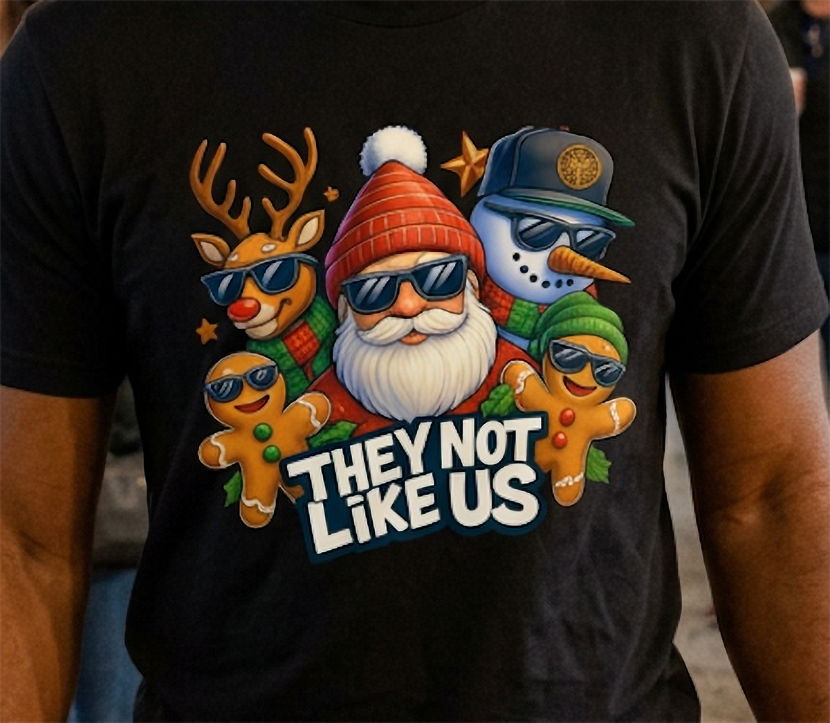 Close-up of black They Not Like Us Christmas shirt showing colorful Santa, reindeer, snowman, and gingerbread holiday graphic.