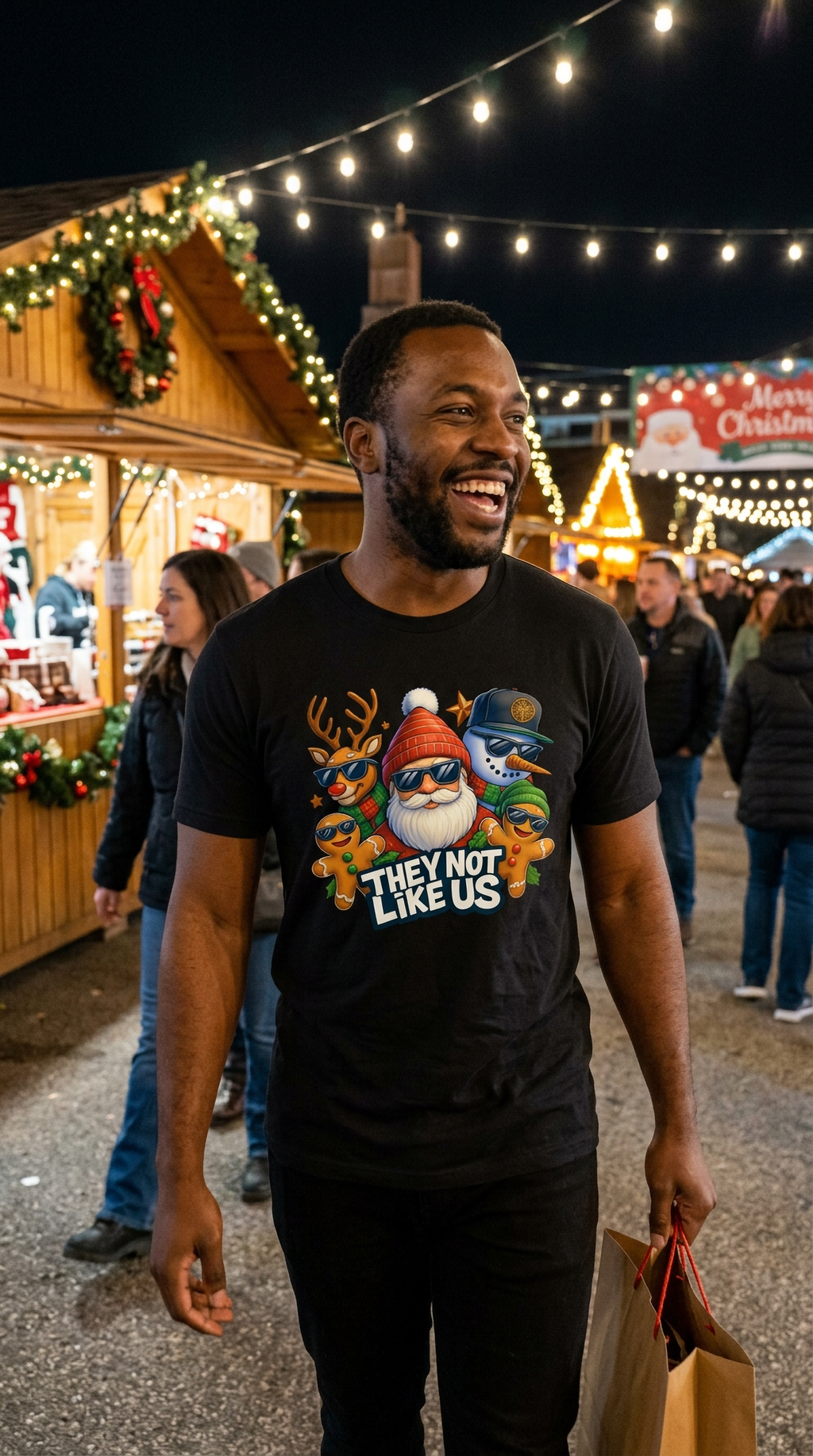 Man wearing black They Not Like Us Christmas graphic t-shirt while walking through an outdoor Christmas market decorated with holiday lights.