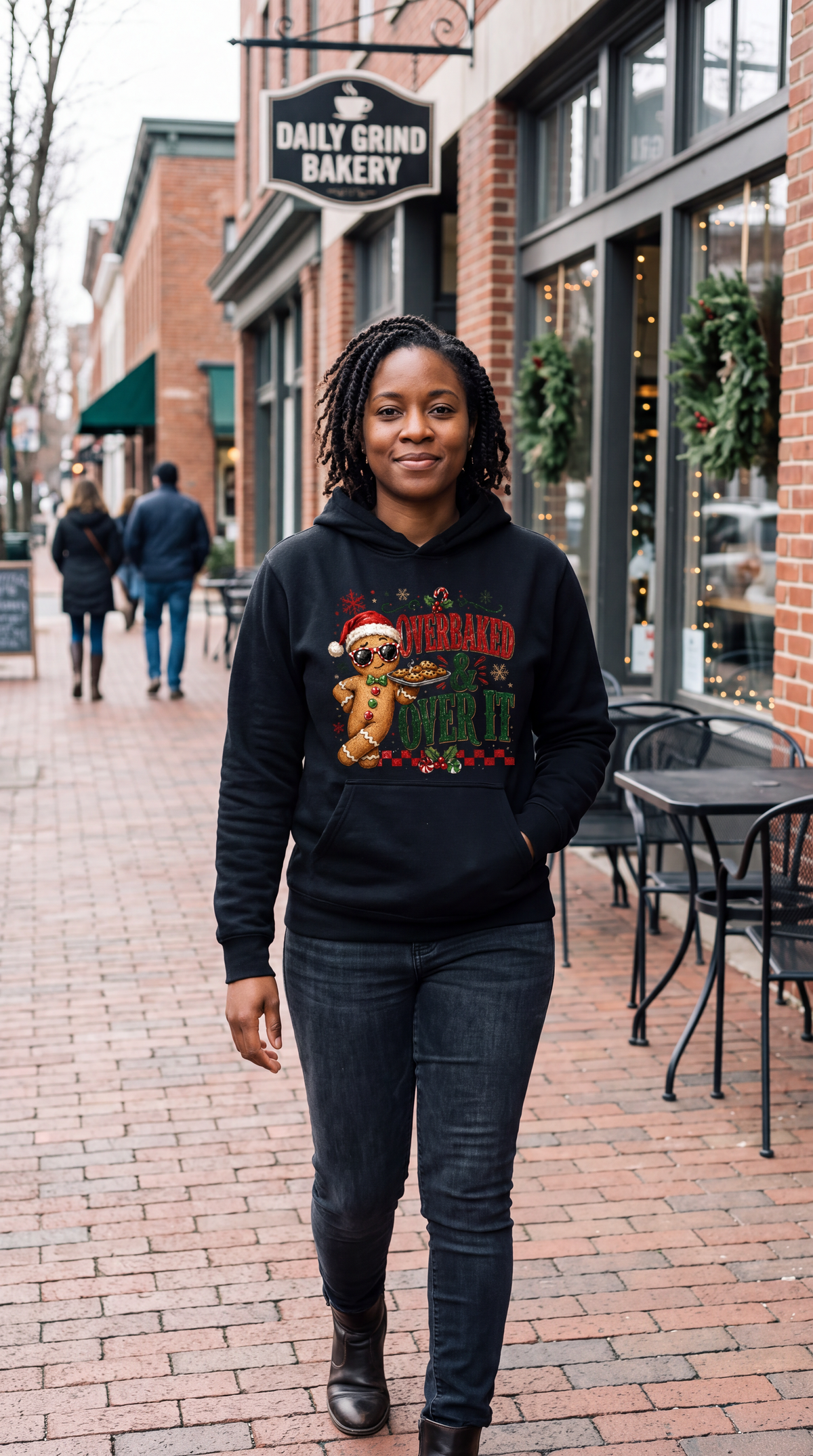 Woman wearing black funny gingerbread Christmas hoodie with Overbaked and Over It design