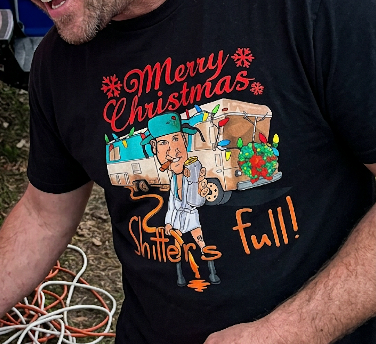 Black Design Close-Up: Close-up of black Christmas Vacation-inspired t-shirt featuring a humorous camper illustration, colorful holiday lights, and Shitter's Full lettering.