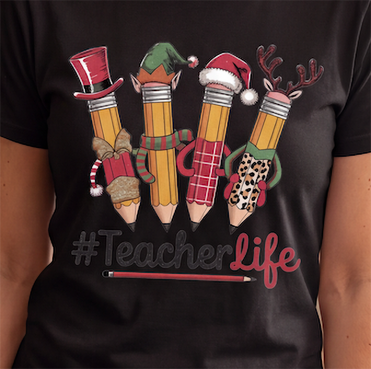 Close-up of black Teacher Life Christmas shirt showing festive character pencils and #TeacherLife lettering.