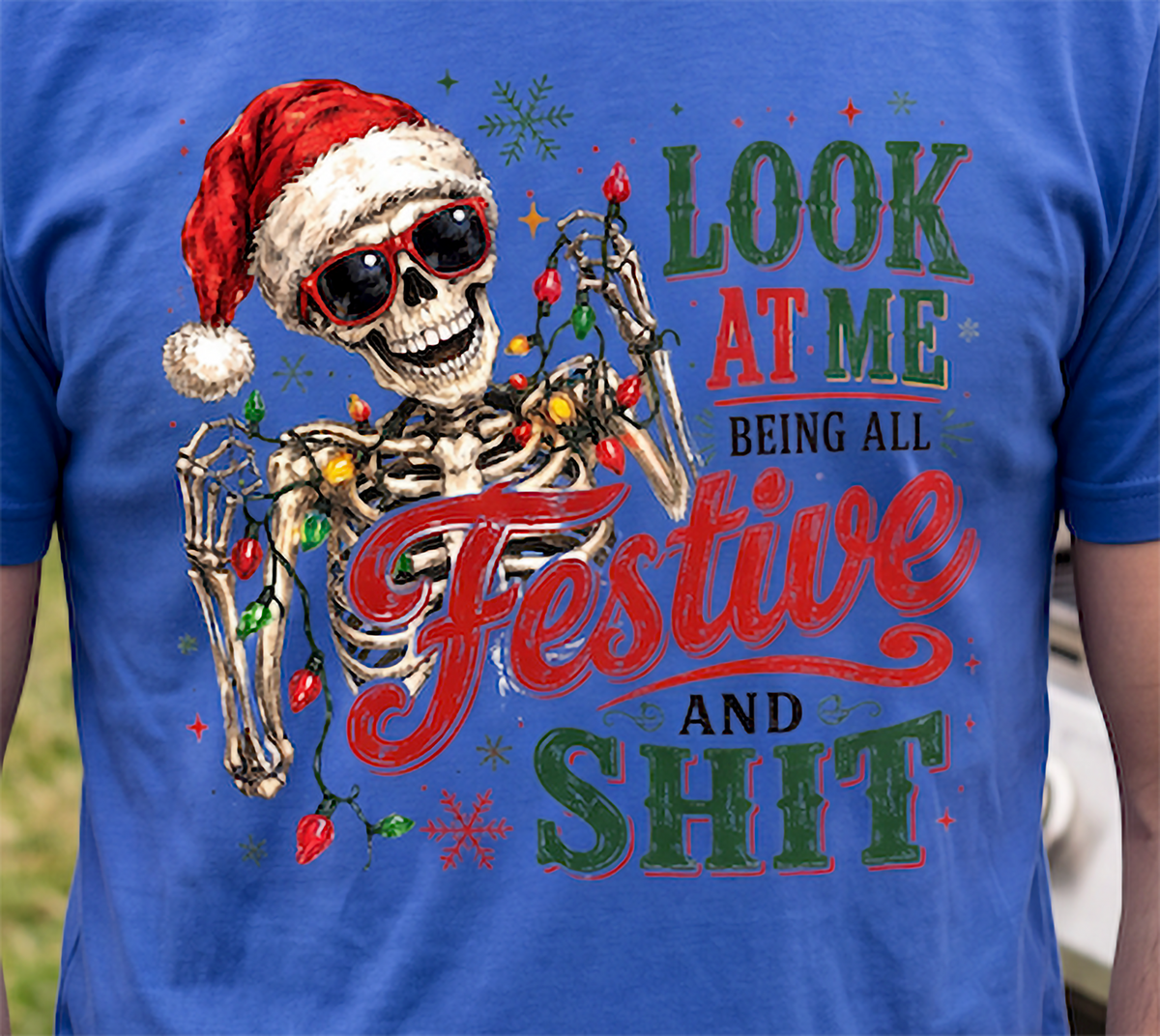 Blue close-up: Close-up of funny Santa skeleton Christmas graphic with colorful lights printed on blue shirt.