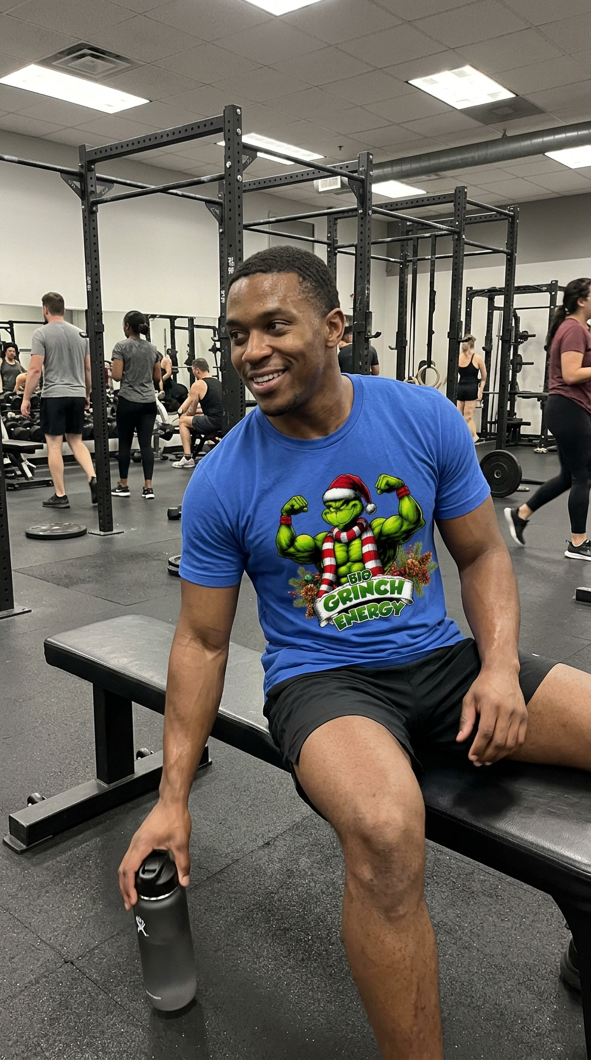Man wearing blue Big Grinch Energy Christmas t-shirt at the gym featuring funny muscular Grinch Christmas artwork.