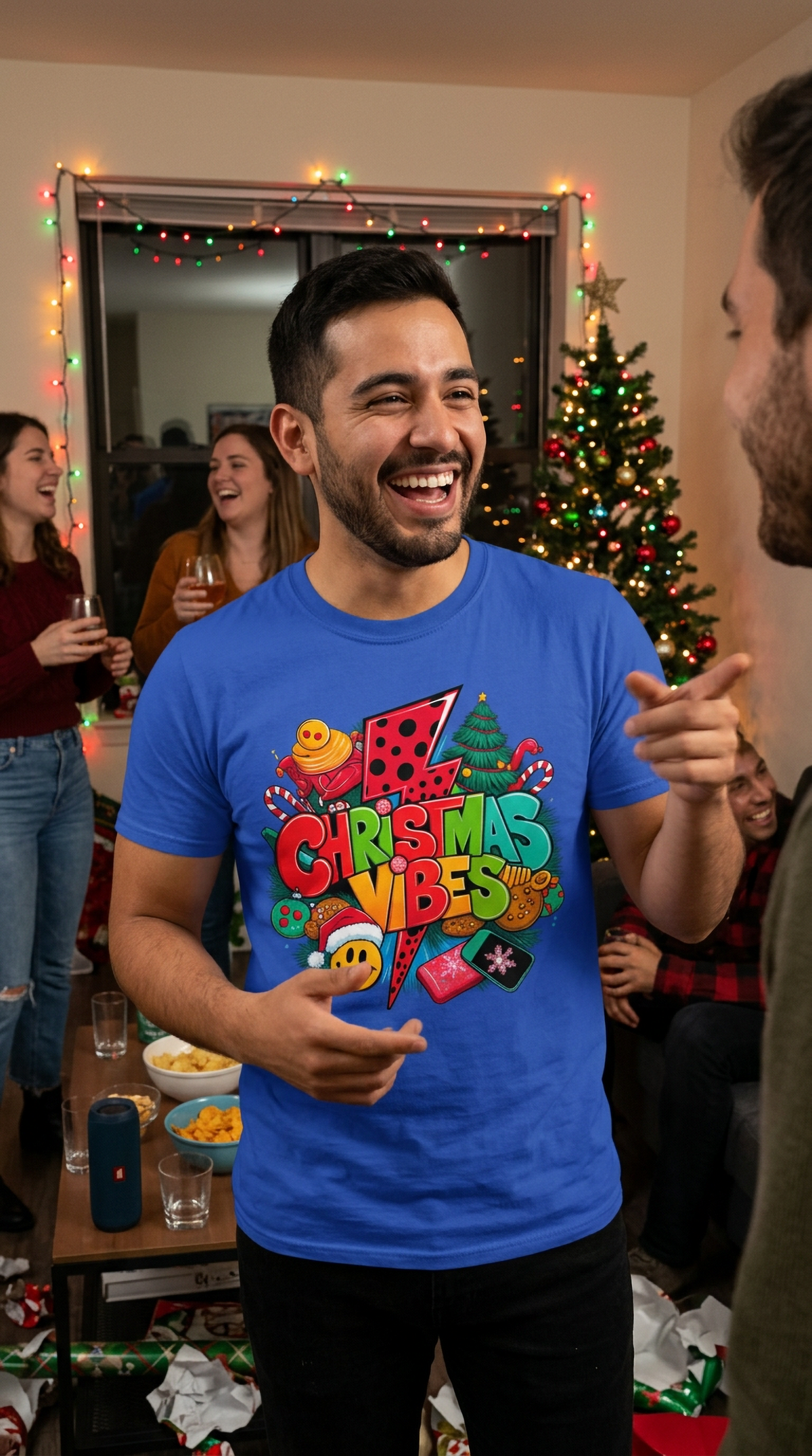 Lifestyle – Blue: Man wearing a blue Christmas Vibes graphic t-shirt at an indoor holiday gathering, displaying colorful retro Christmas artwork.