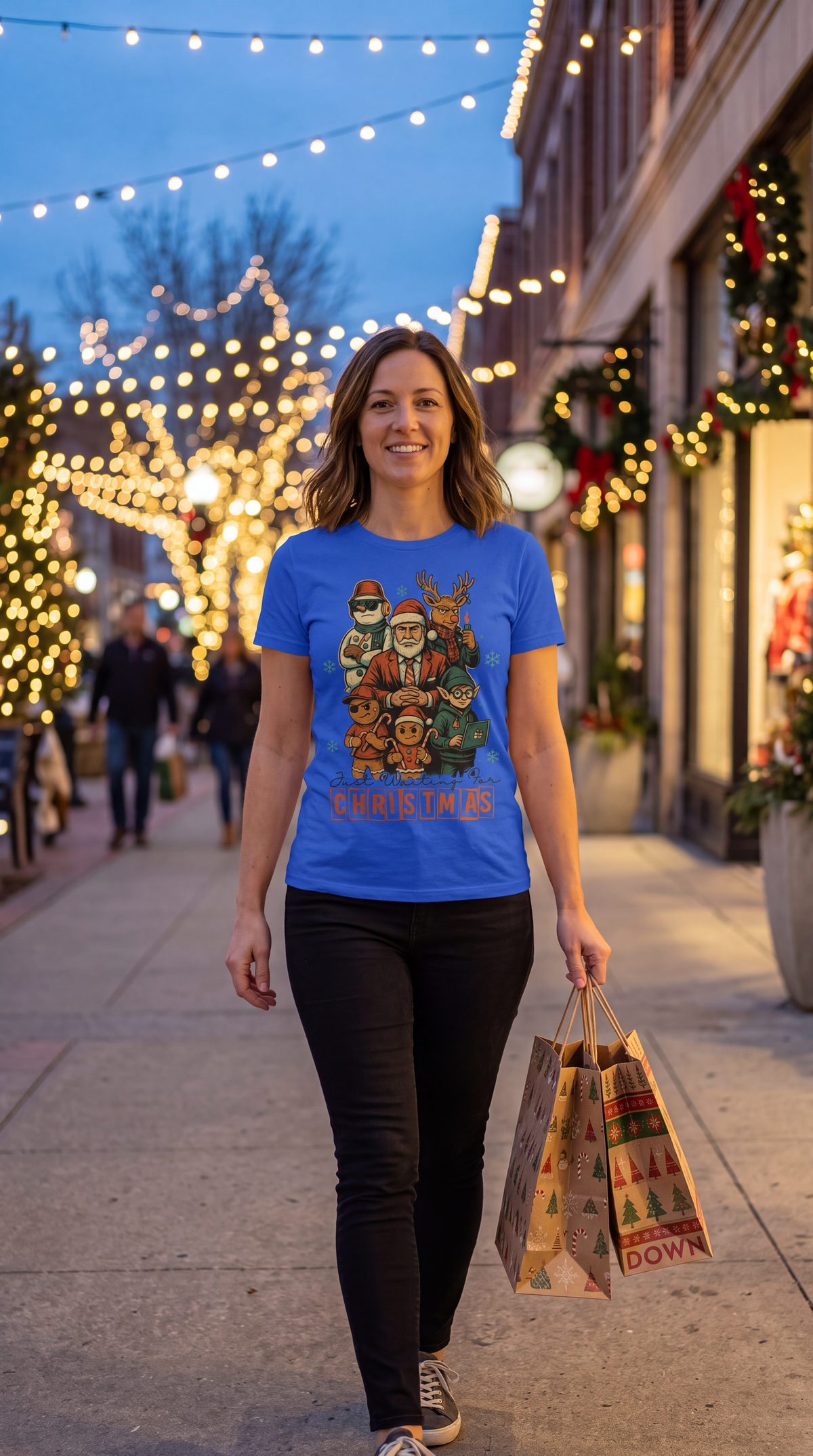Woman wearing royal blue funny Christmas graphic tee featuring Santa, reindeer, elf, snowman and gingerbread characters.