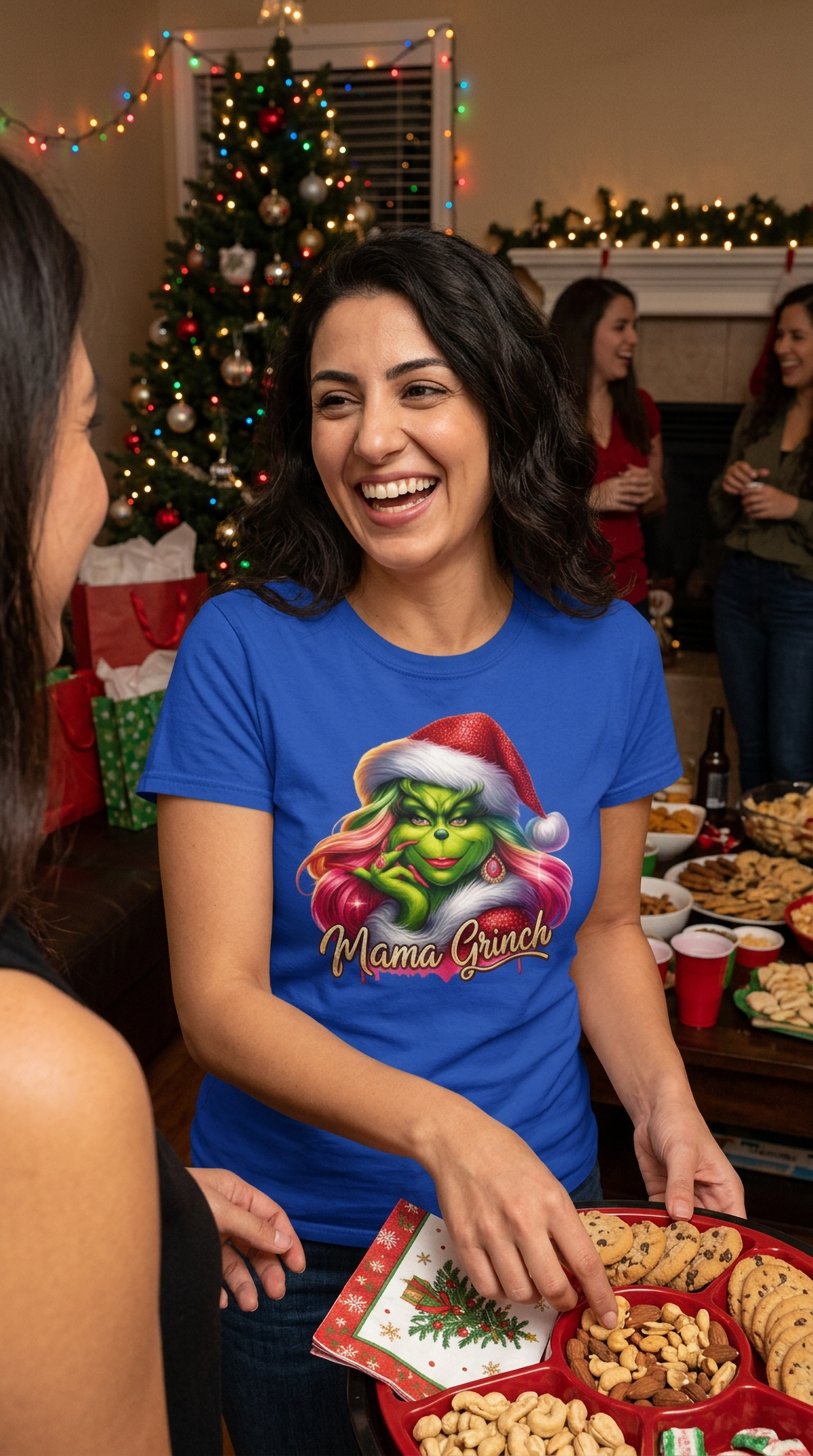 Smiling woman wearing blue Mama Grinch Christmas shirt while sitting with holiday gifts at a festive gathering.