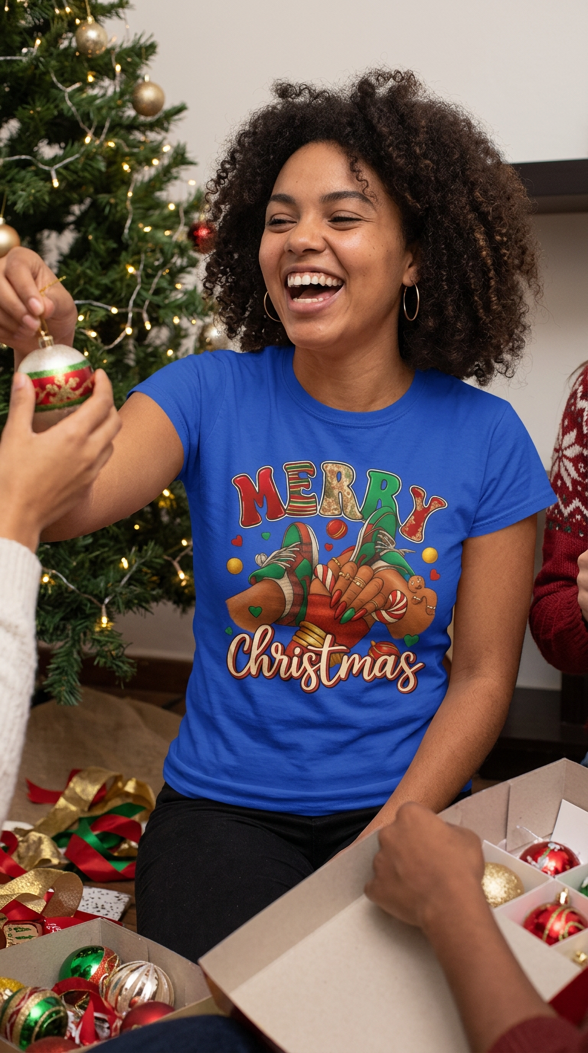 Lifestyle – Blue: Woman wearing a blue Merry Christmas sneaker graphic t-shirt while celebrating the holidays near a decorated Christmas tree
