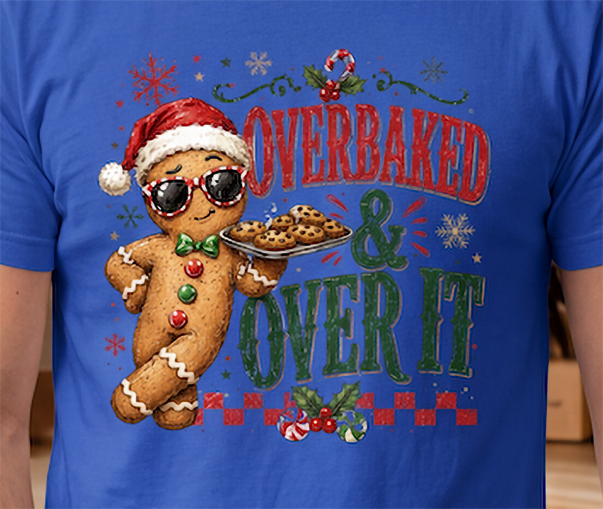 Close-up of Overbaked and Over It gingerbread Christmas graphic printed on blue shirt.